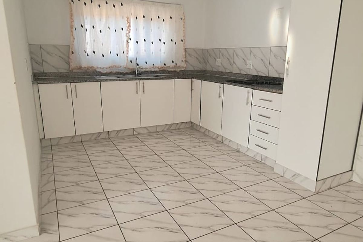 A clean, modern kitchen featuring white cabinetry, granite countertops, a double basin sink, and marble-look ceramic floor tiles.