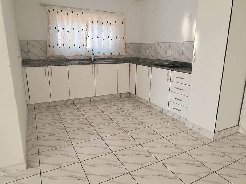 A clean, modern kitchen featuring white cabinetry, granite countertops, a double basin sink, and marble-look ceramic floor tiles.