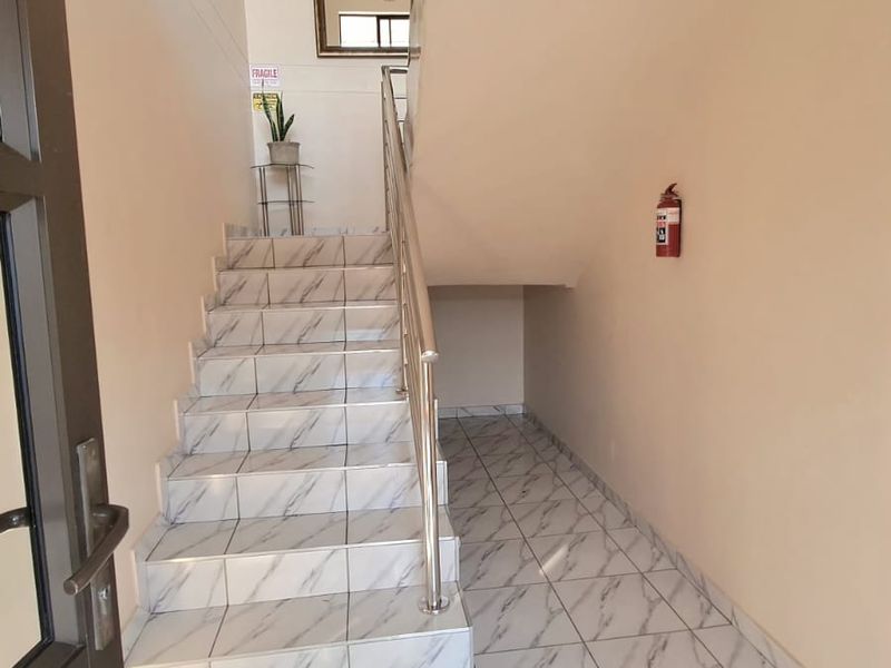 A clean, well-lit entrance area featuring marble-effect tiled flooring and a staircase with a modern stainless steel handrail.