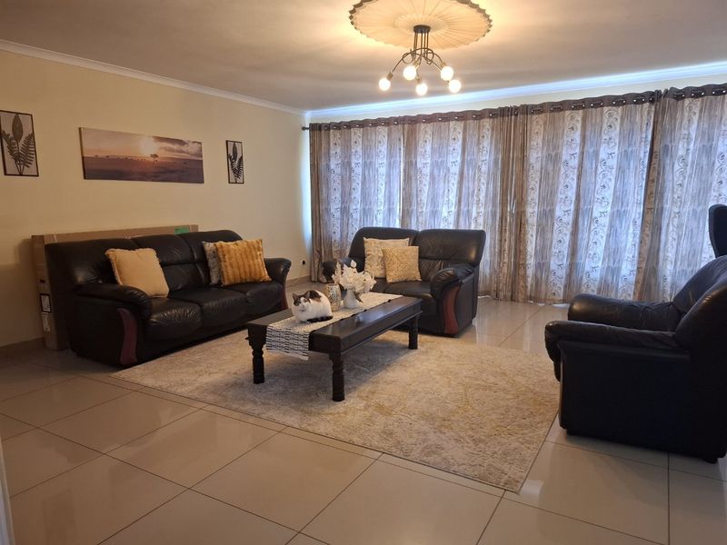 A spacious living room featuring large format floor tiles, a decorative ceiling rose, and floor-to-ceiling sliding glass doors with curtains.