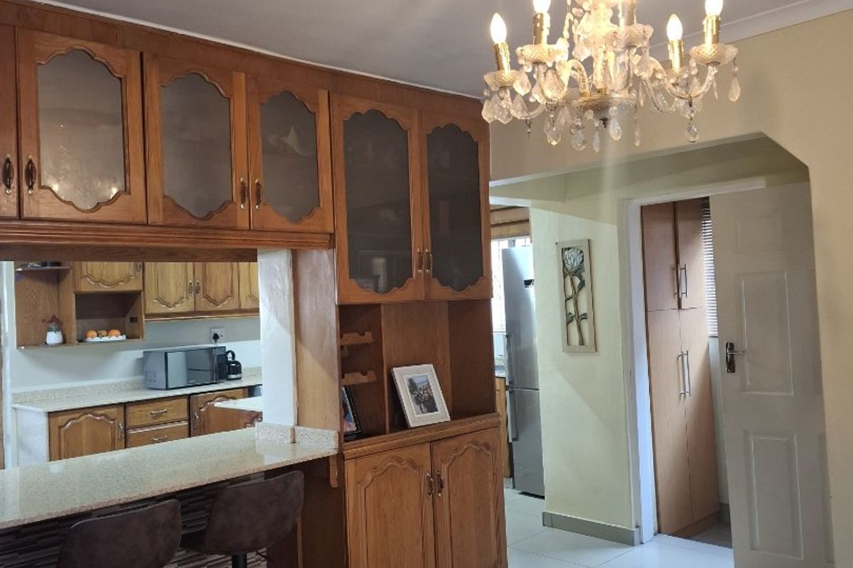 A kitchen featuring wooden cabinetry, a granite breakfast bar, and tiled flooring, complemented by a decorative ceiling rose and chandelier.