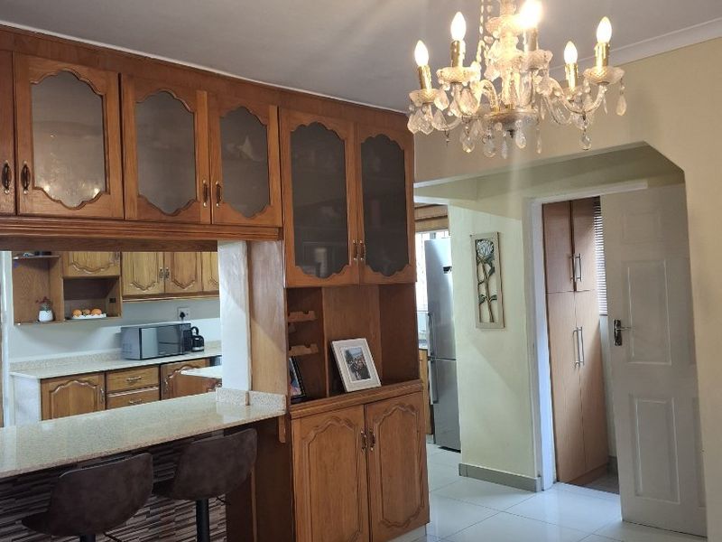 A kitchen featuring wooden cabinetry, a granite breakfast bar, and tiled flooring, complemented by a decorative ceiling rose and chandelier.