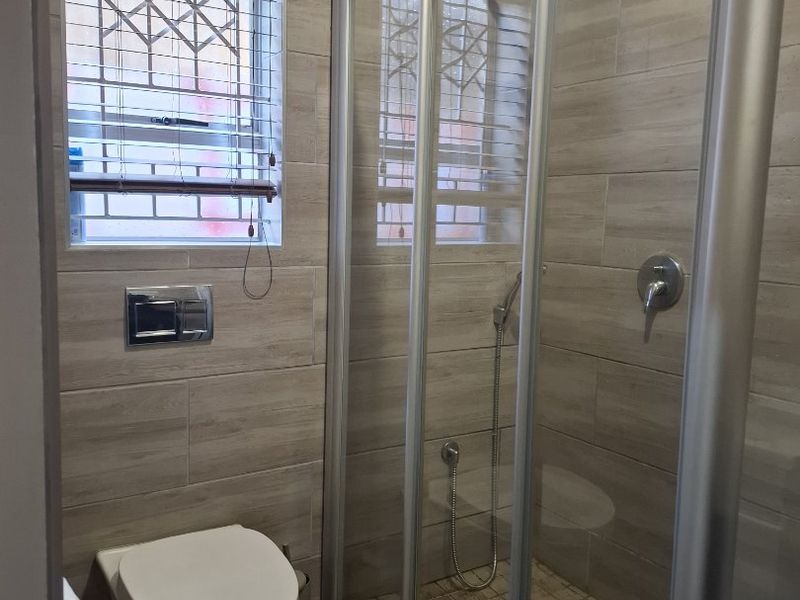 Modern bathroom featuring a walk-in shower with glass enclosure, wall-mounted toilet with concealed cistern, and neutral wood-look tiled finishes.