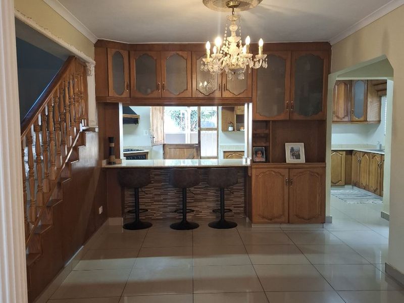 Open plan living area featuring a wooden staircase, tiled flooring, and a breakfast bar with built-in cabinetry connecting to the kitchen space.