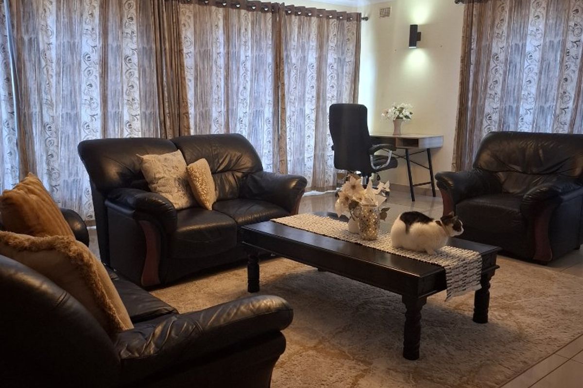 Spacious living room featuring tiled flooring, a decorative ceiling rose with modern lighting, and large windows with floor-to-ceiling curtains.