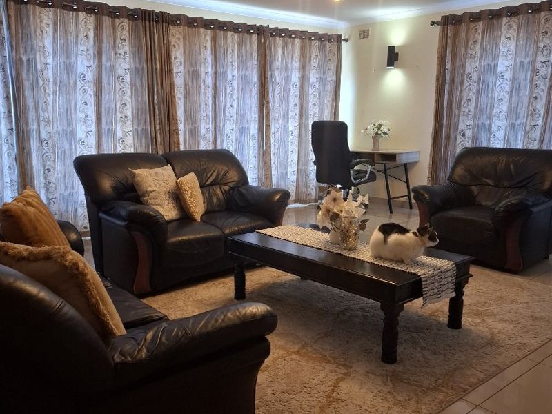 Spacious living room featuring tiled flooring, a decorative ceiling rose with modern lighting, and large windows with floor-to-ceiling curtains.