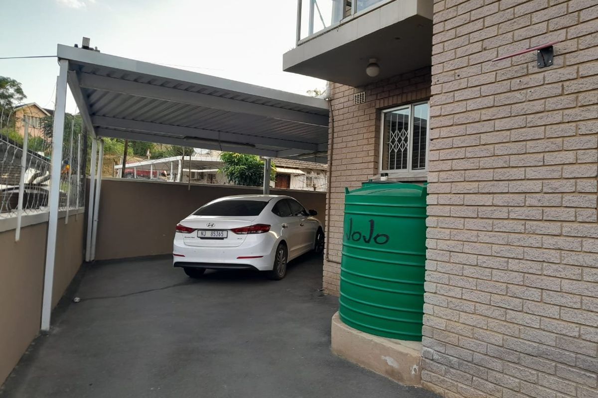 Rear exterior area featuring a covered carport, paved driveway, and a large water storage tank against the brick building facade.