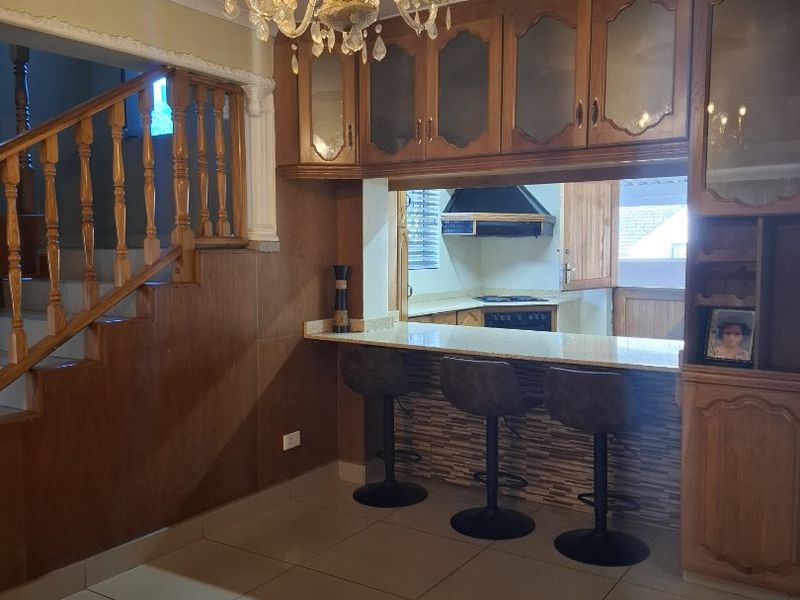 Open plan kitchen and dining area featuring wooden cabinetry, a stone breakfast bar, and a classic crystal chandelier, adjacent to a wooden staircase.