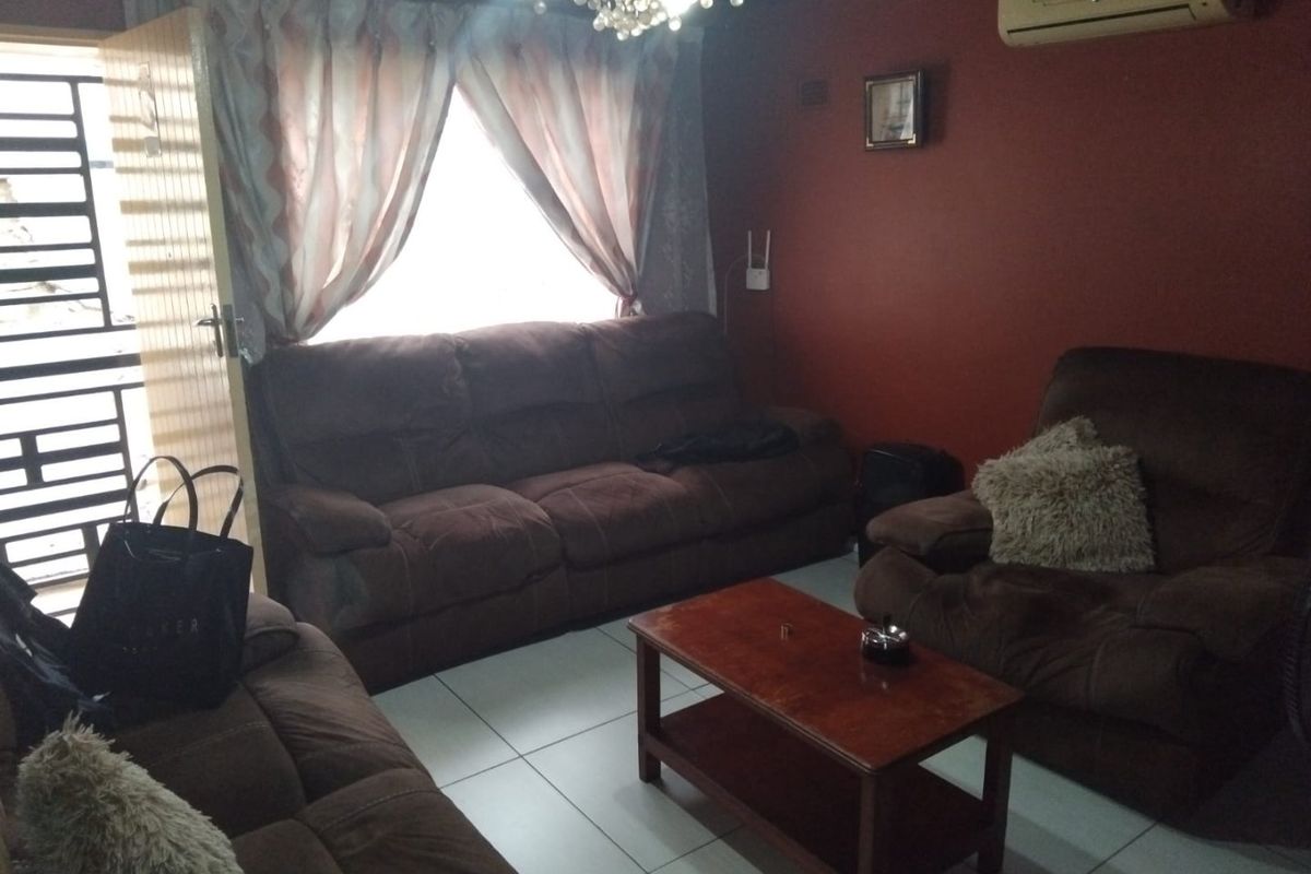 A living room featuring tiled flooring, a wall-mounted air conditioning unit, and a security gate at the entrance.