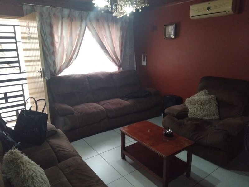A living room featuring tiled flooring, a wall-mounted air conditioning unit, and a security gate at the entrance.