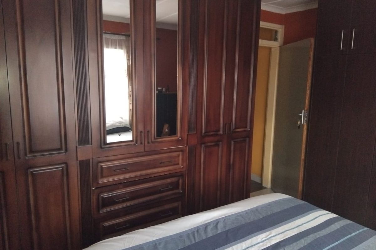 A bedroom featuring extensive dark wood built-in cupboards with integrated mirrored panels and drawers, providing ample storage space.