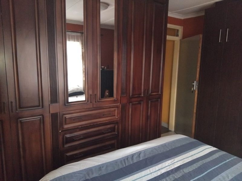 A bedroom featuring extensive dark wood built-in cupboards with integrated mirrored panels and drawers, providing ample storage space.