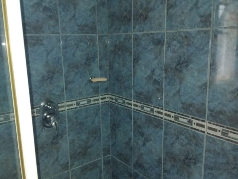 A shower enclosure featuring blue patterned wall tiles, a chrome shower mixer, and a fixed shower head.