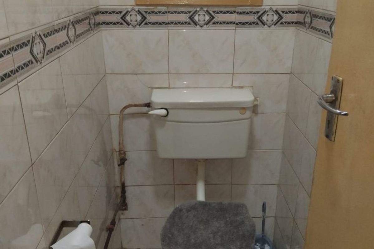 A compact bathroom featuring tiled walls and floors, a standard toilet with a high-level cistern, and a small window with security bars.