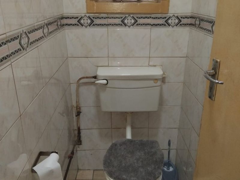 A compact bathroom featuring tiled walls and floors, a standard toilet with a high-level cistern, and a small window with security bars.