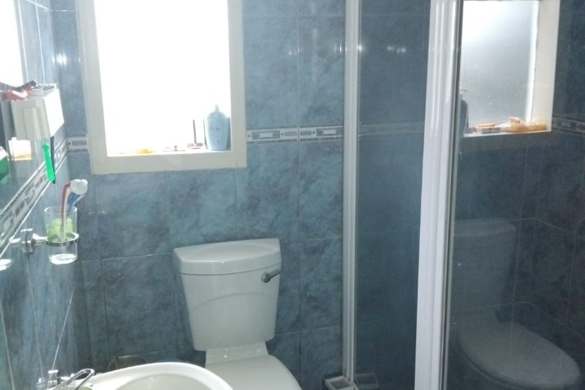A functional bathroom featuring blue wall and floor tiles, a pedestal washbasin, a toilet, and a glass-enclosed shower unit.