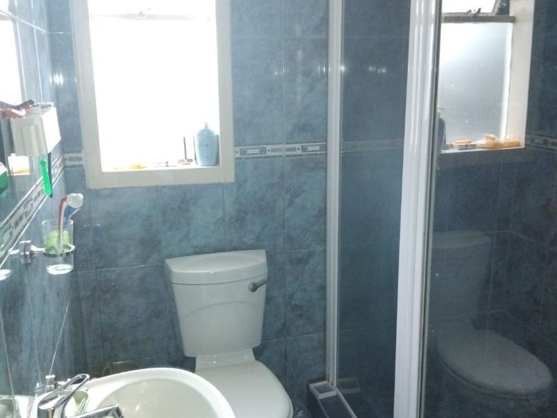 A functional bathroom featuring blue wall and floor tiles, a pedestal washbasin, a toilet, and a glass-enclosed shower unit.