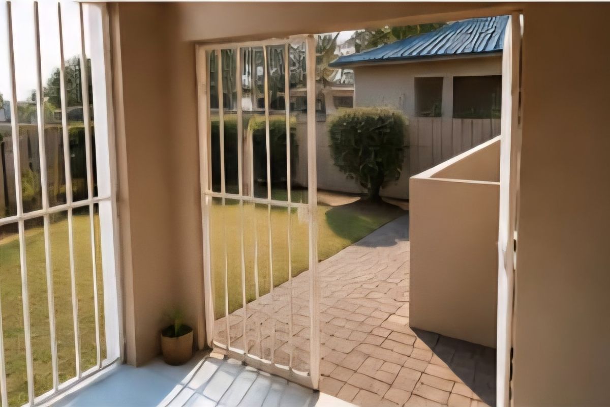 A covered patio area featuring security bars, leading out to a paved walkway and a private garden space.