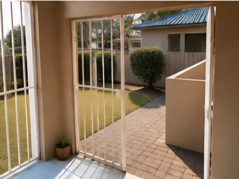 A covered patio area featuring security bars, leading out to a paved walkway and a private garden space.