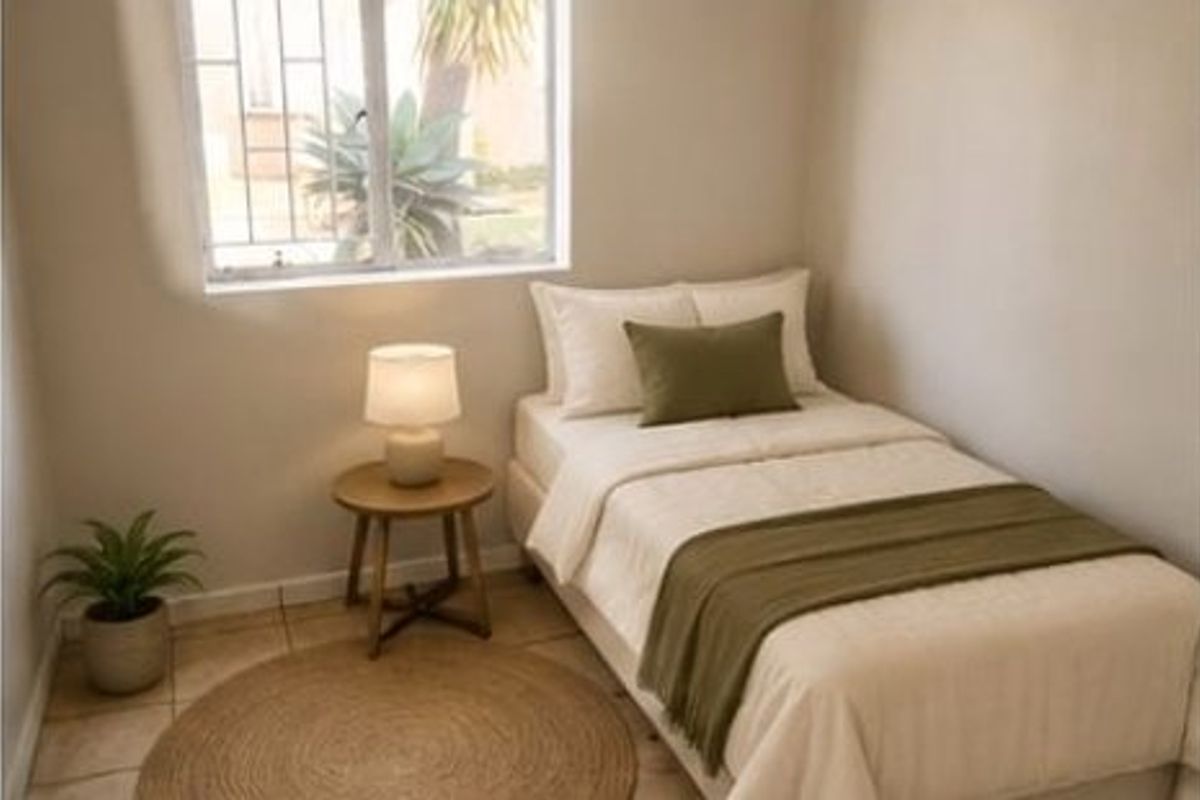 A compact bedroom featuring tiled flooring and a window fitted with security bars, providing natural light.