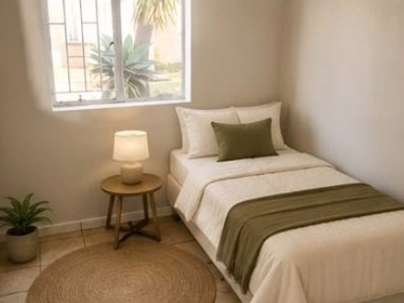 A compact bedroom featuring tiled flooring and a window fitted with security bars, providing natural light.