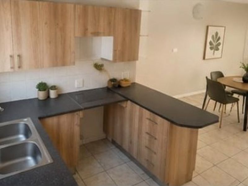Open plan kitchen featuring light wood-look cabinetry, dark laminate countertops, and a double bowl sink, seamlessly flowing into the adjacent dining area.