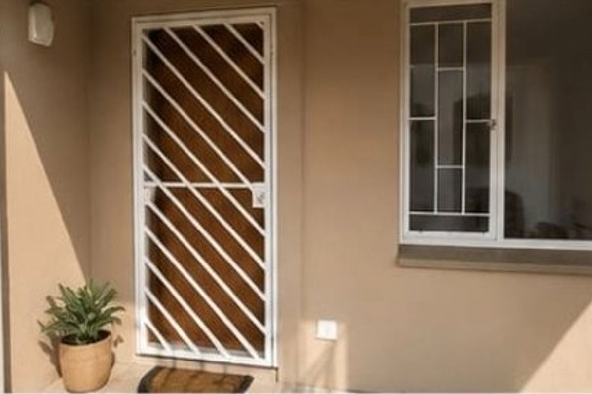 A clean apartment entrance featuring a white security gate and matching window security bars on a neutral-toned exterior wall.