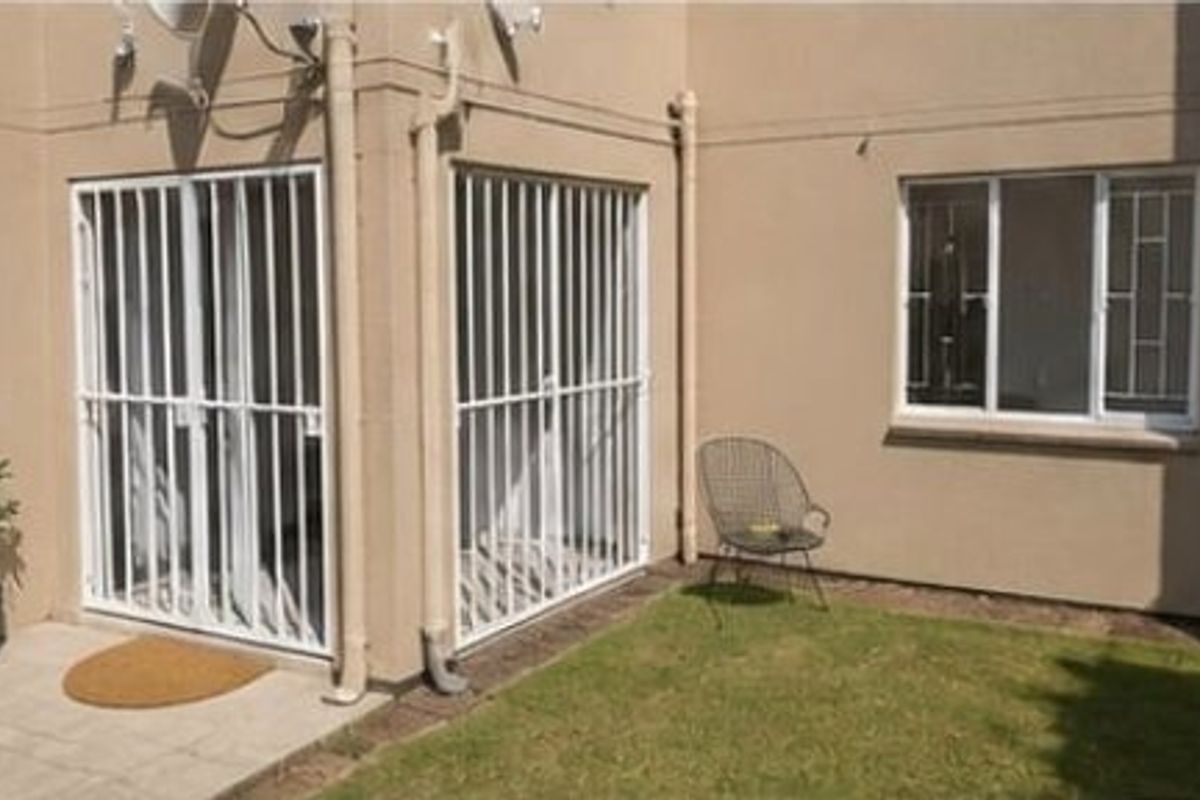 Rear exterior view of the apartment featuring a small paved patio area, security gates, and security bars on the windows.