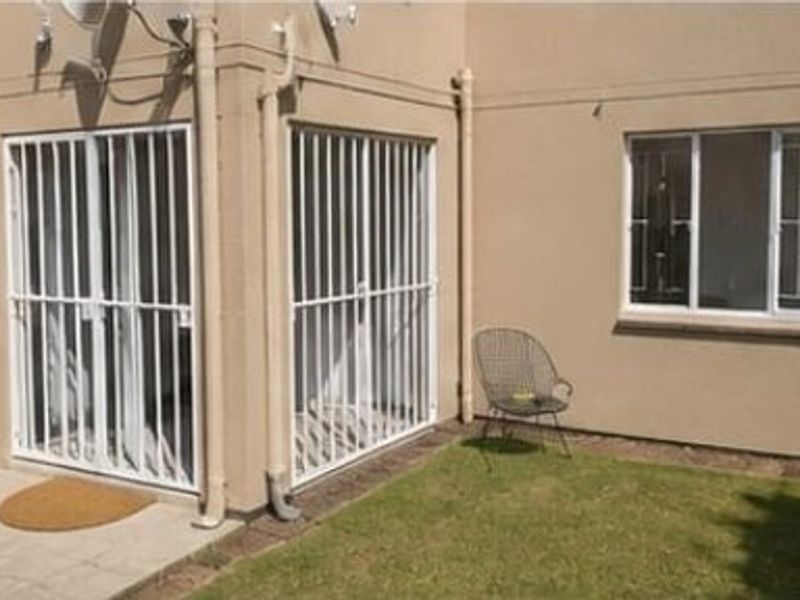 Rear exterior view of the apartment featuring a small paved patio area, security gates, and security bars on the windows.