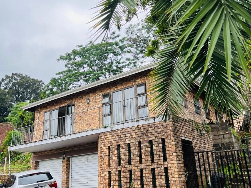 Two-story face brick residential property featuring a double garage, upper-level balcony with metal railings, and established surrounding greenery.