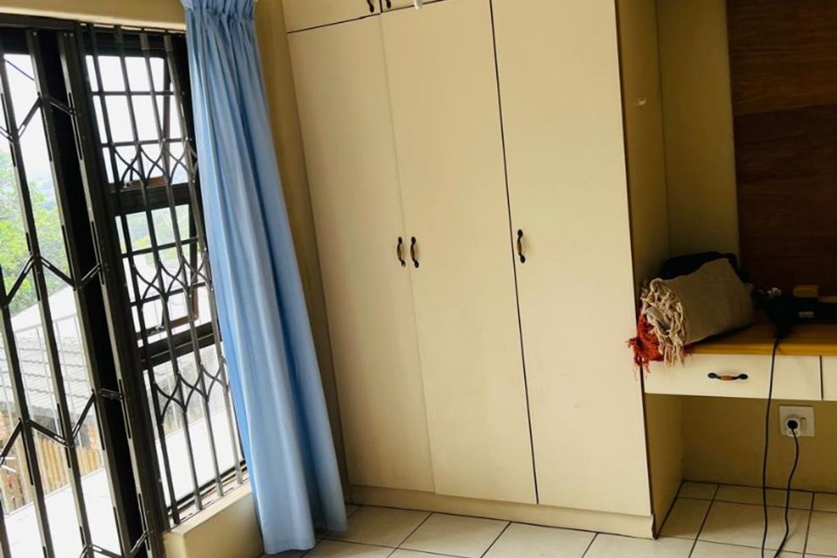Bedroom featuring built-in cupboards, a built-in desk, tiled flooring, and a security gate on the window.