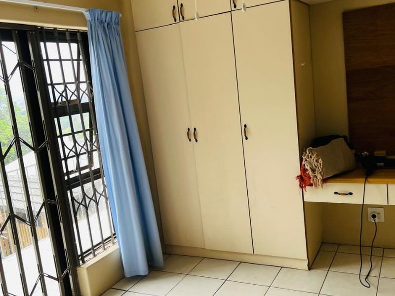 Bedroom featuring built-in cupboards, a built-in desk, tiled flooring, and a security gate on the window.