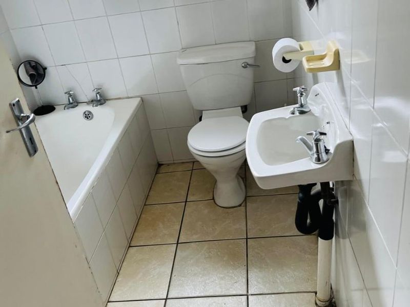A compact bathroom featuring a bathtub, toilet, and wall-mounted basin with tiled finishes throughout.