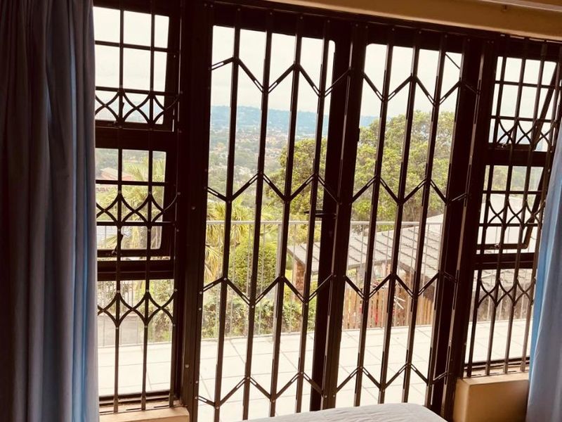 A bedroom featuring large windows with security gates, offering natural light and views of the surrounding area.