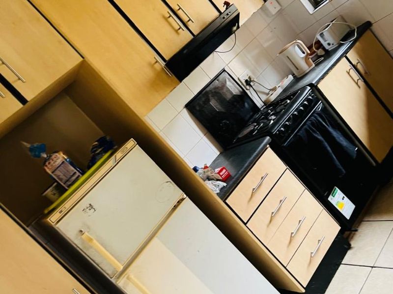 A compact kitchen featuring light wood-finish cabinetry, tiled backsplash, and tiled flooring. The space requires cosmetic updates to modernize the dated finishes.