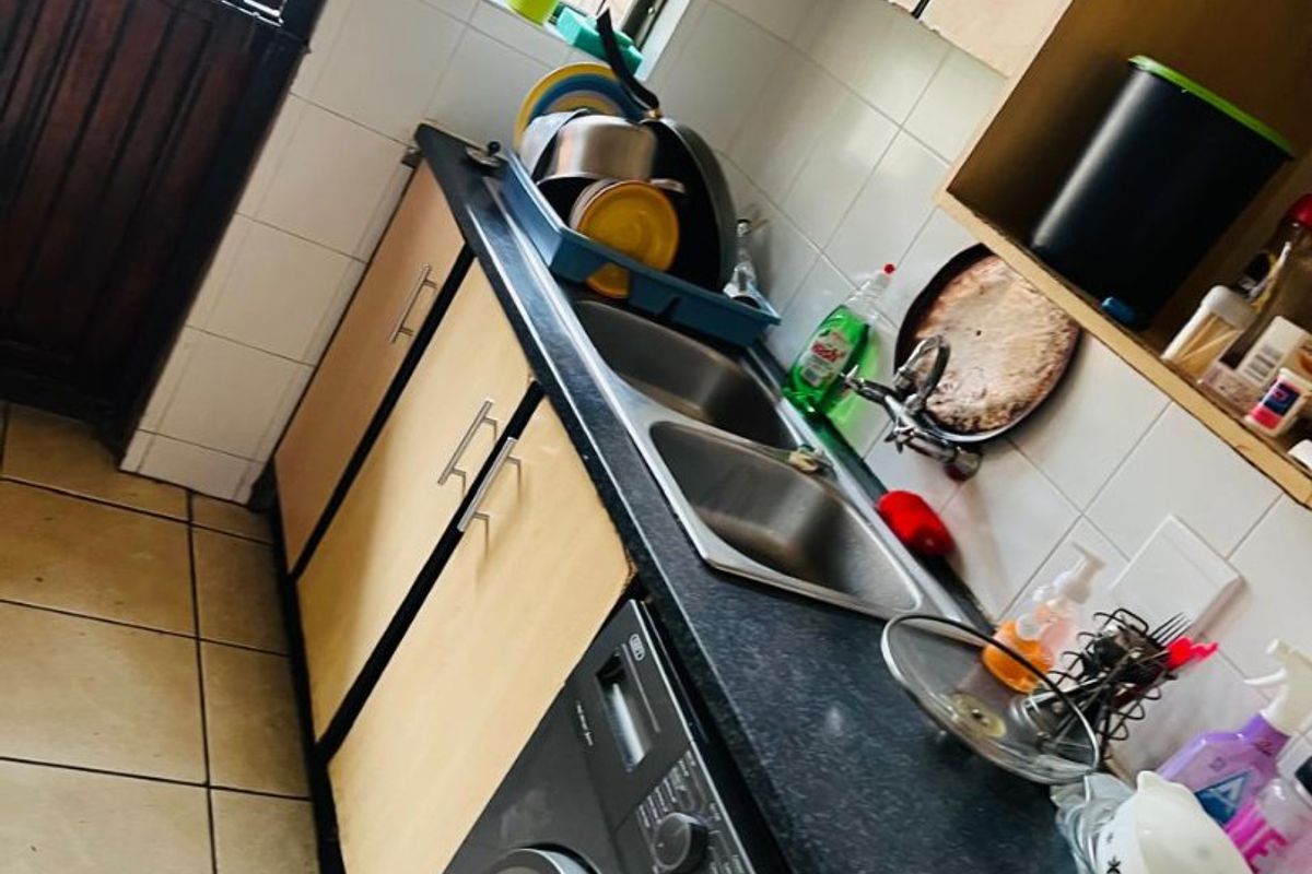 A functional kitchen area featuring laminate cabinetry, a double bowl stainless steel sink, tiled splashbacks, and tiled flooring with an integrated washing machine space.