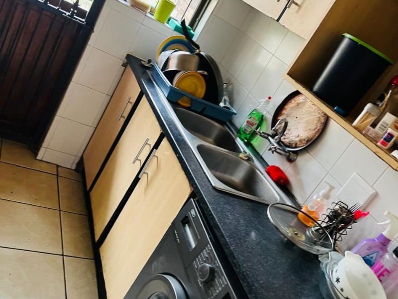 A functional kitchen area featuring laminate cabinetry, a double bowl stainless steel sink, tiled splashbacks, and tiled flooring with an integrated washing machine space.