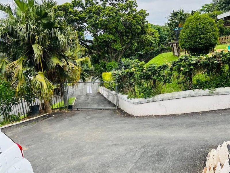 A view of the property entrance featuring an asphalt driveway, a metal security gate, and a landscaped garden with a retaining wall.