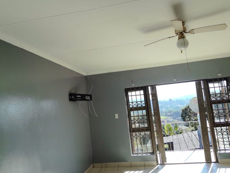 An empty living room featuring tiled floors, a ceiling fan, and a sliding door leading to a balcony with scenic views.