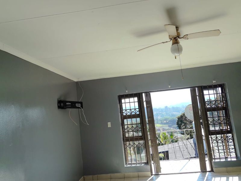An empty living room featuring tiled floors, a ceiling fan, and a sliding door with security gates leading to an outdoor balcony.
