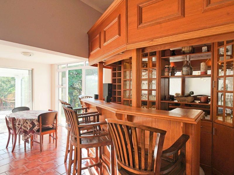 A dedicated home bar area featuring extensive built-in wooden cabinetry, glass shelving, and tiled flooring with direct access to an outdoor patio.