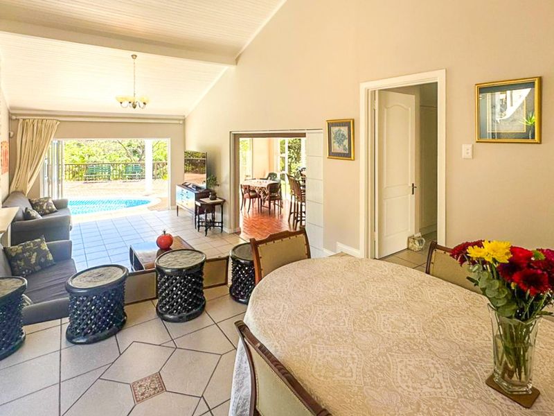 Spacious open-plan living and dining area featuring vaulted ceilings, tiled floors, and seamless access to the outdoor patio and pool area.