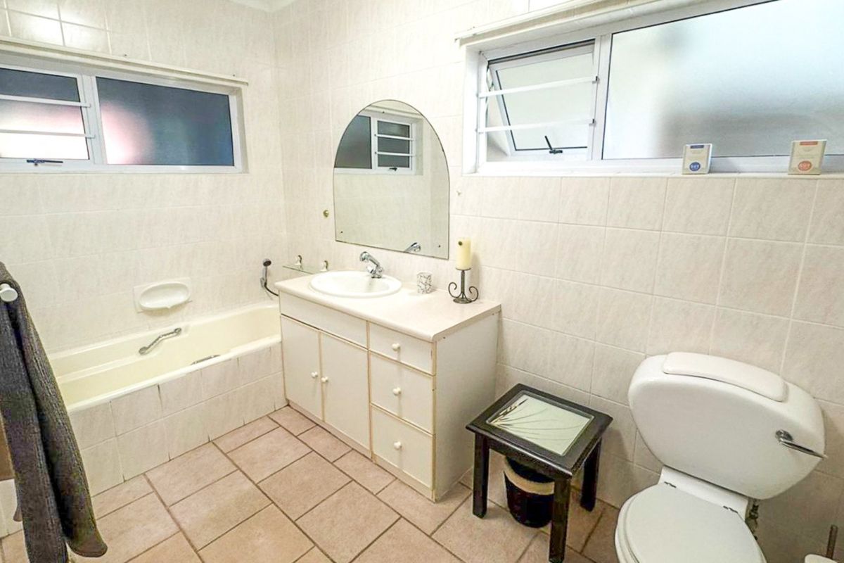 A functional bathroom featuring a built-in vanity, bathtub, toilet, and tiled surfaces throughout, offering a dated but well-maintained layout.