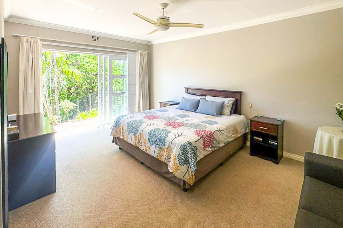 Spacious bedroom featuring neutral carpeting, a ceiling fan, and large sliding glass doors providing direct access to the outdoor area.