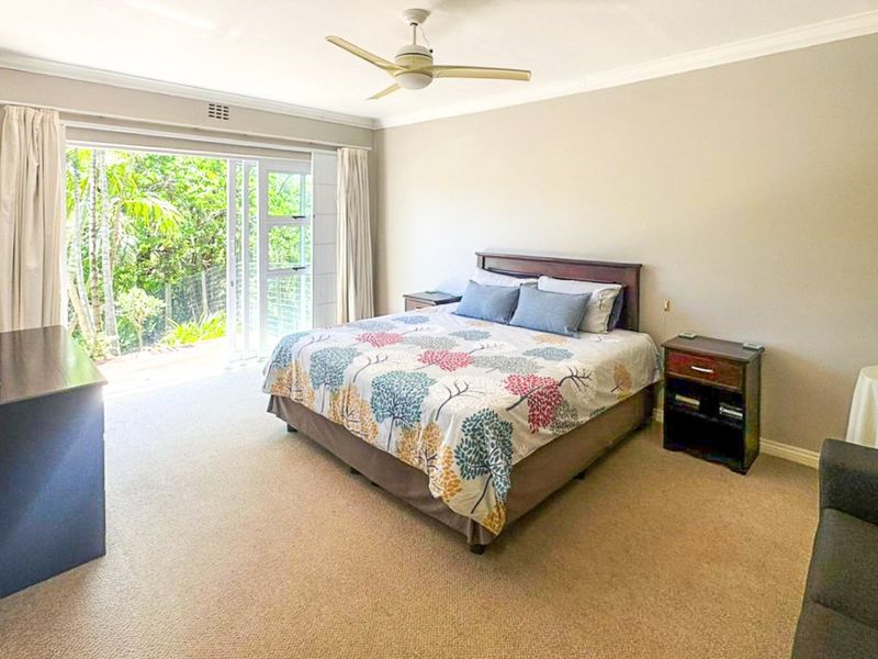 Spacious bedroom featuring neutral carpeting, a ceiling fan, and large sliding glass doors providing direct access to the outdoor area.