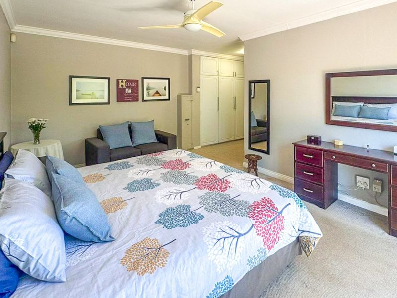 A spacious bedroom featuring neutral wall tones, carpeted flooring, a ceiling fan, and ample built-in cupboard storage.