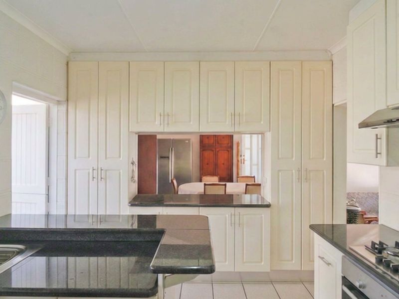 A functional kitchen featuring cream cabinetry, dark granite countertops, a gas hob, built-in oven, and a stainless steel extractor fan.