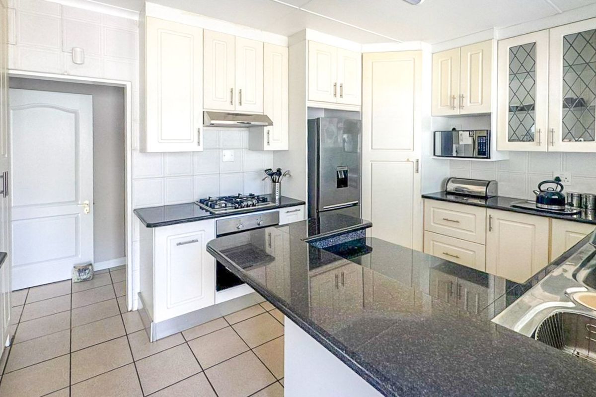 A well-maintained kitchen featuring cream cabinetry, dark granite countertops, a gas hob, built-in oven, and tiled flooring with a functional layout.
