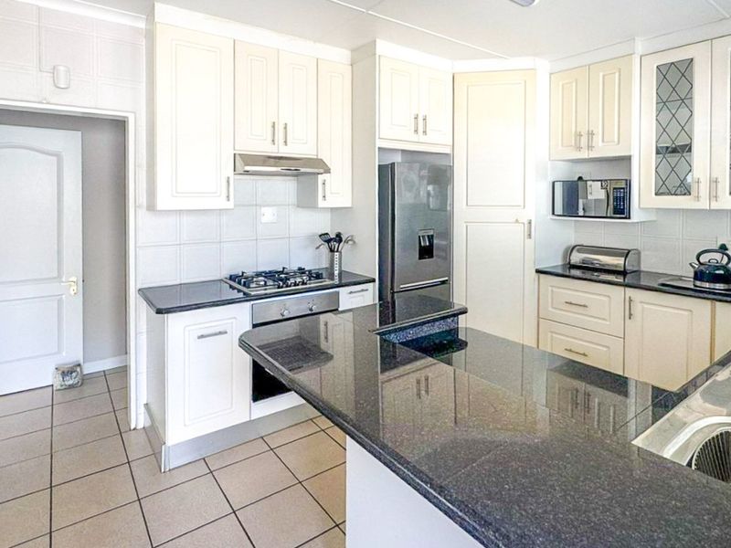 A well-maintained kitchen featuring cream cabinetry, dark granite countertops, a gas hob, built-in oven, and tiled flooring with a functional layout.