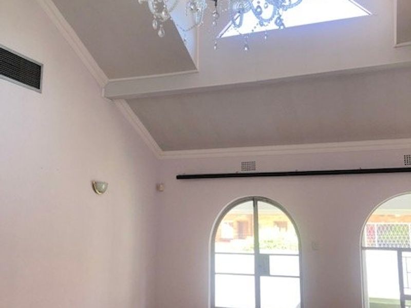 Spacious living area featuring a vaulted ceiling, large skylight, elegant crystal chandelier, and arched glass doors leading to the exterior.